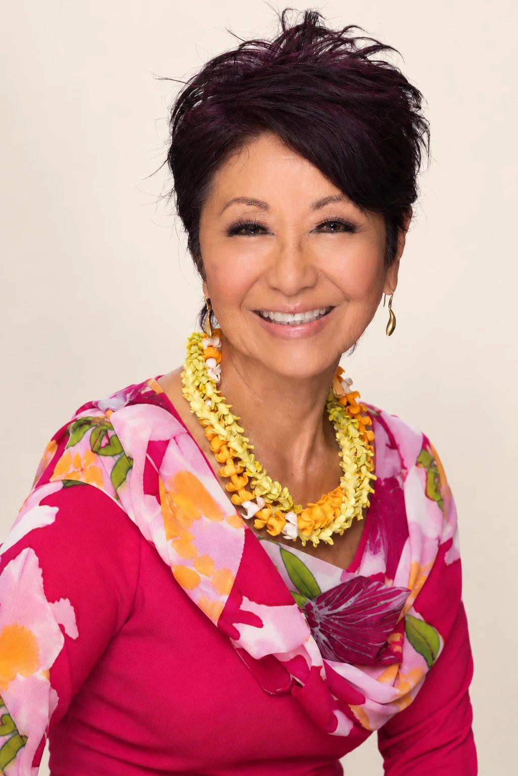 Olelo paʻa Ogawa smiling in a pink floral top and scarf with a yellow and orange lei