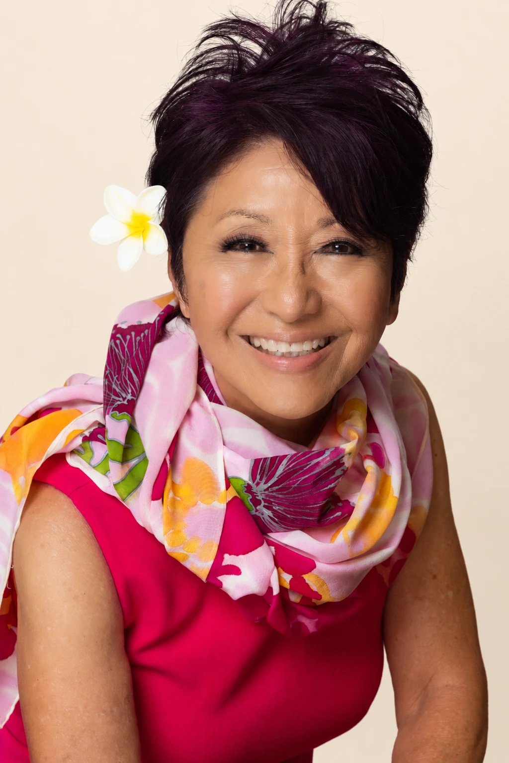 Olelo paʻa Ogawa in a pink dress and floral scarf with a plumeria in her hair
