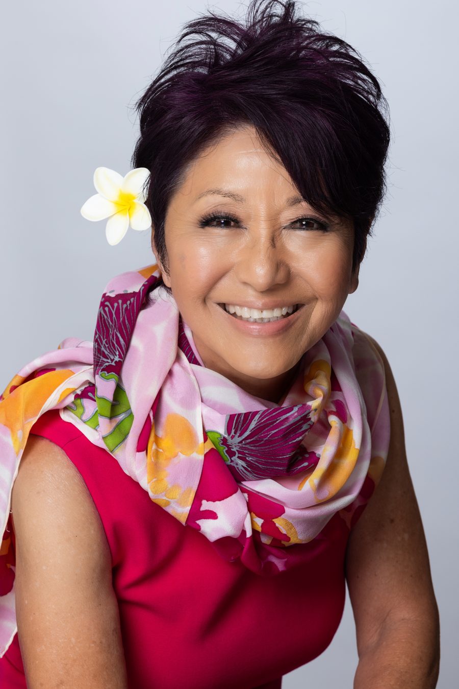 Olelo paʻa Ogawa in a pink dress and floral scarf with a plumeria in her hair