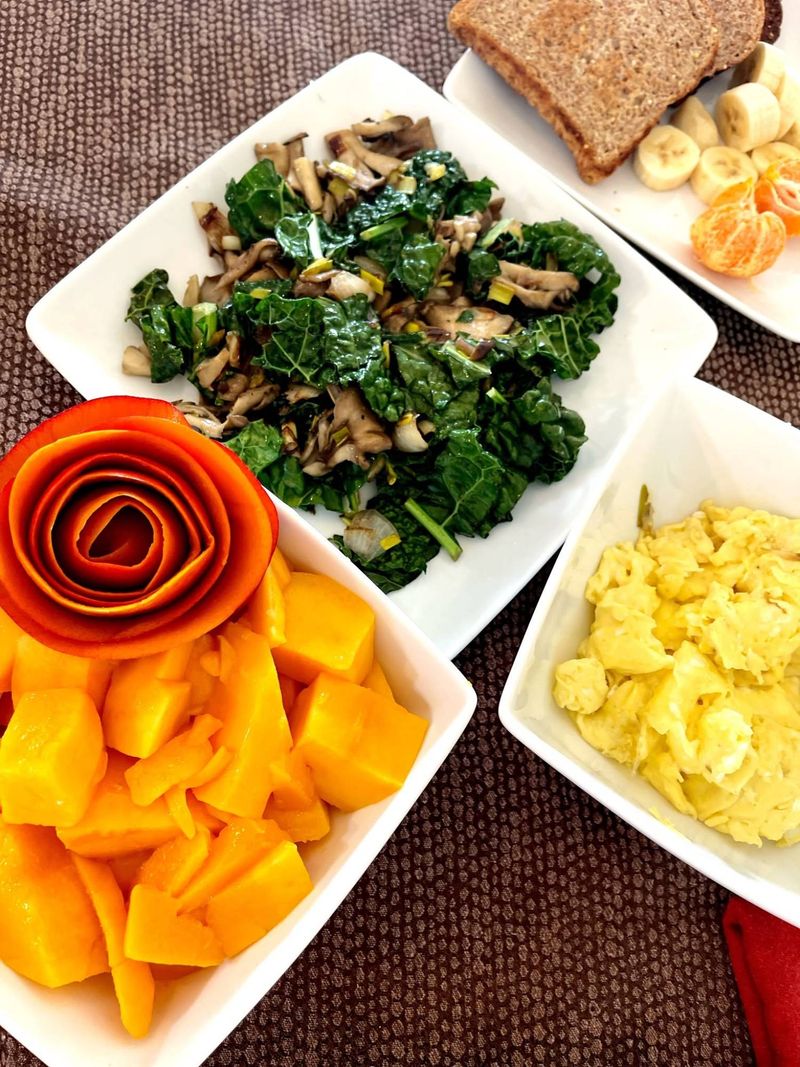 A nourishing breakfast of sautéed kale and mushrooms, eggs, mango and fruit