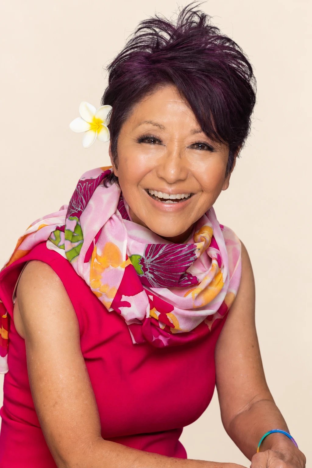 Olelo paʻa laughing in a bright pink dress and floral scarf with a plumeria in her hair