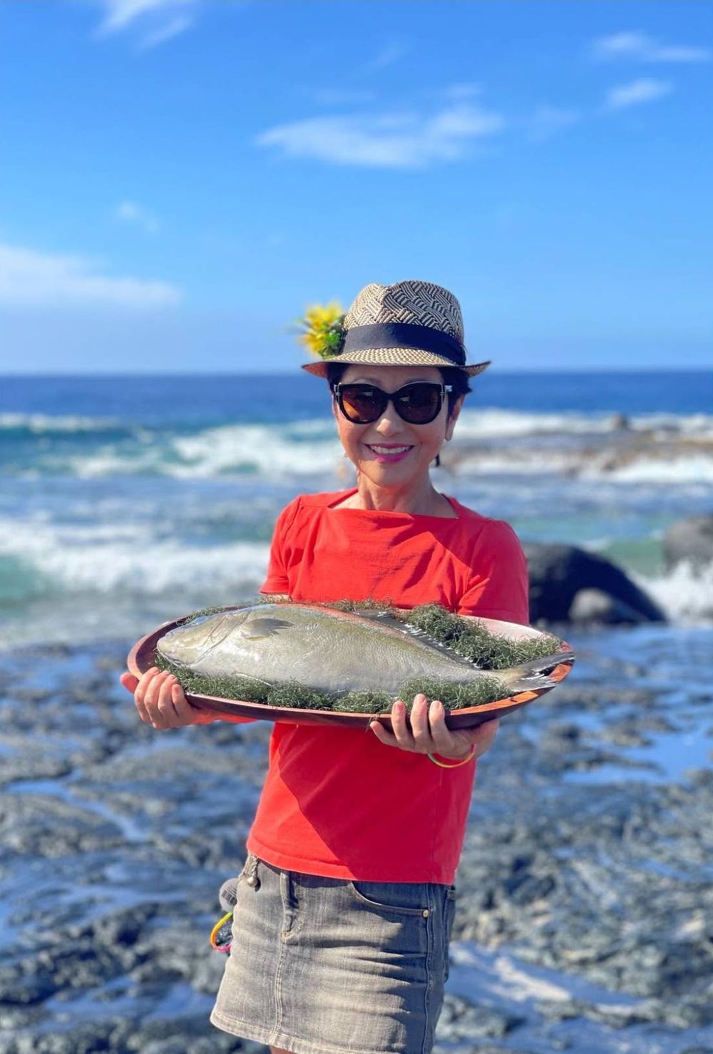 Olelo paʻa by the ocean on Hawaiʻi Island, holding a whole fresh fish on a wooden platter