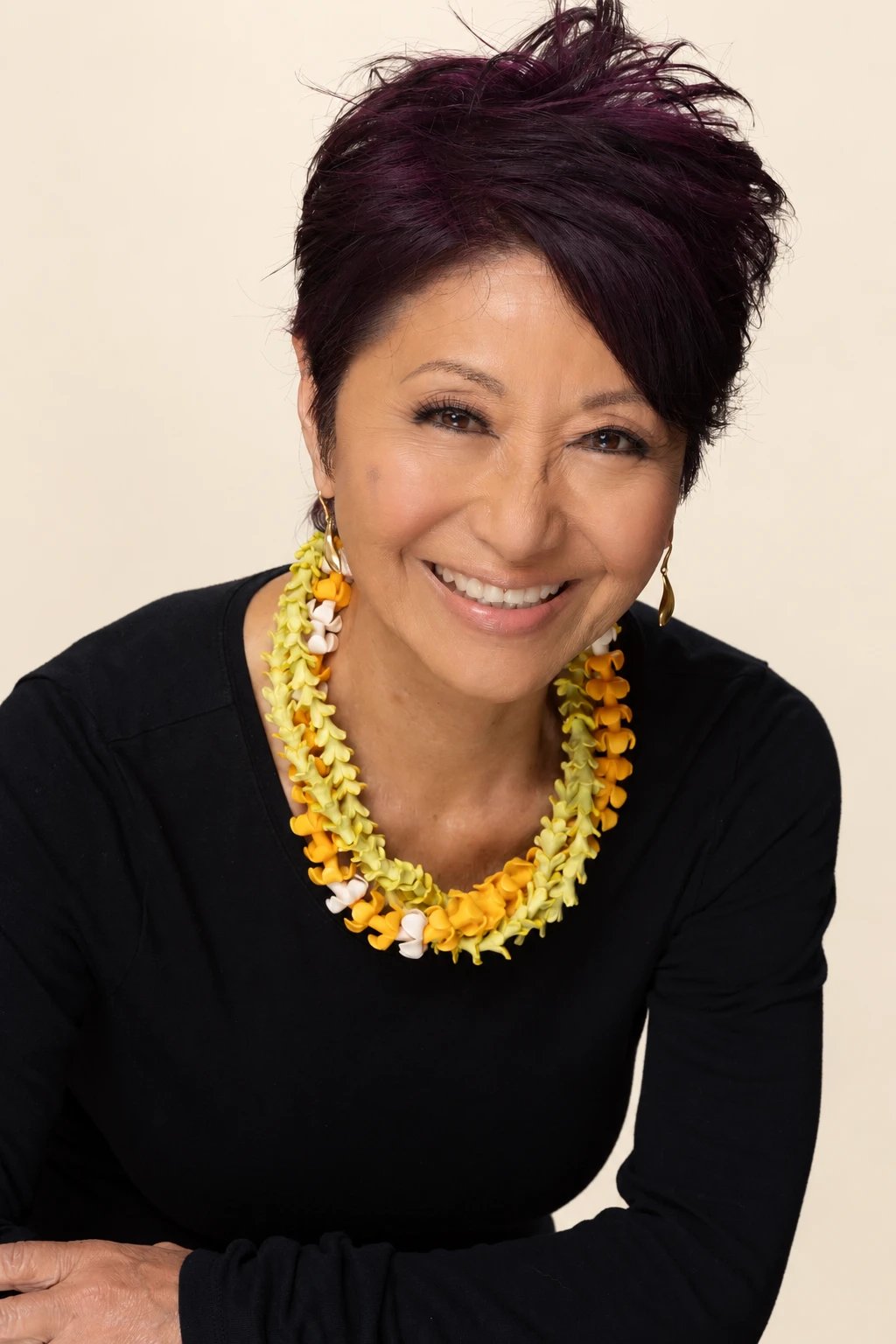 Olelo paʻa Ogawa smiling in a black top with a yellow and orange lei